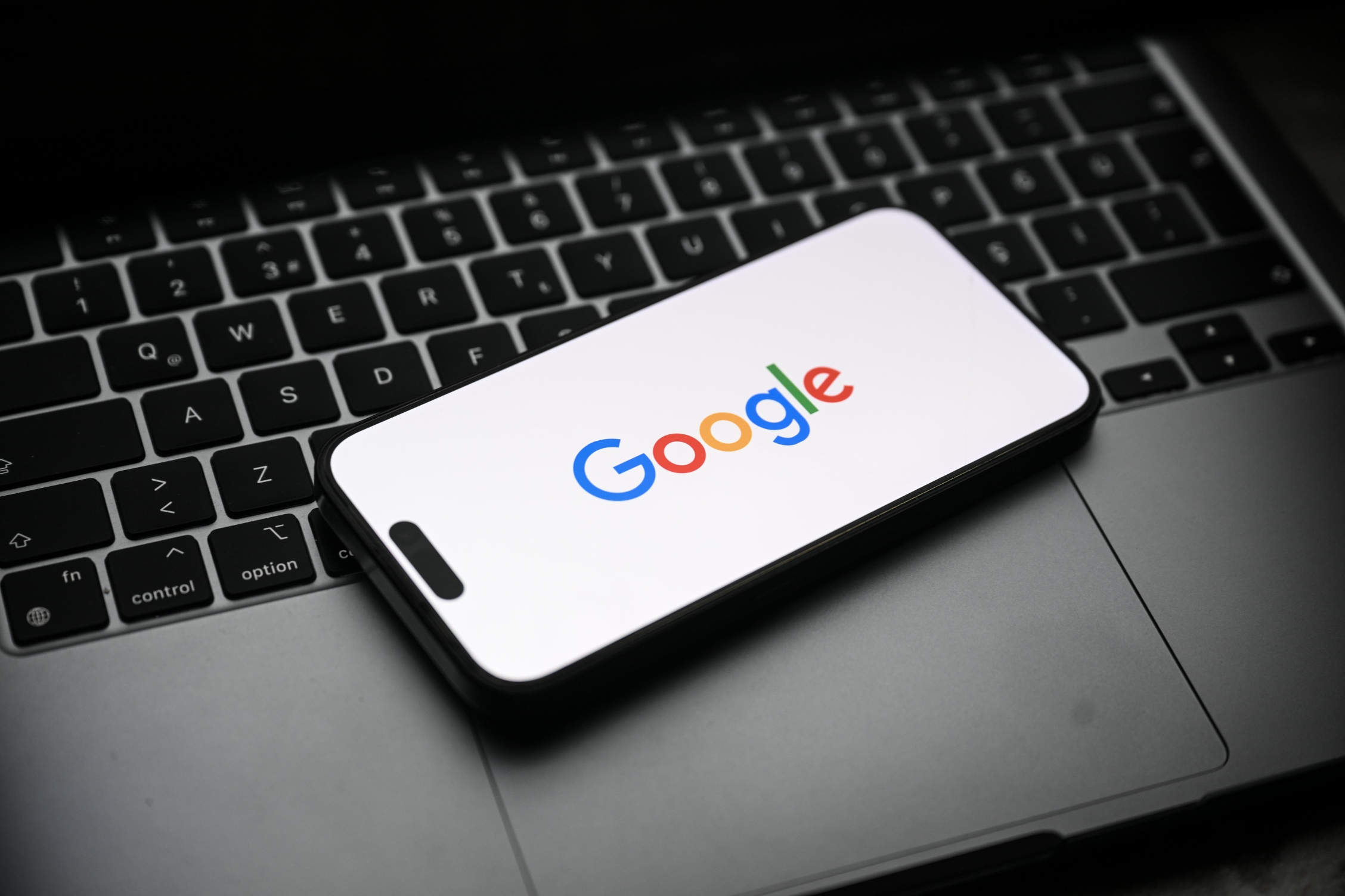 The Google logo displayed on a smartphone that's sitting on top of a laptop.